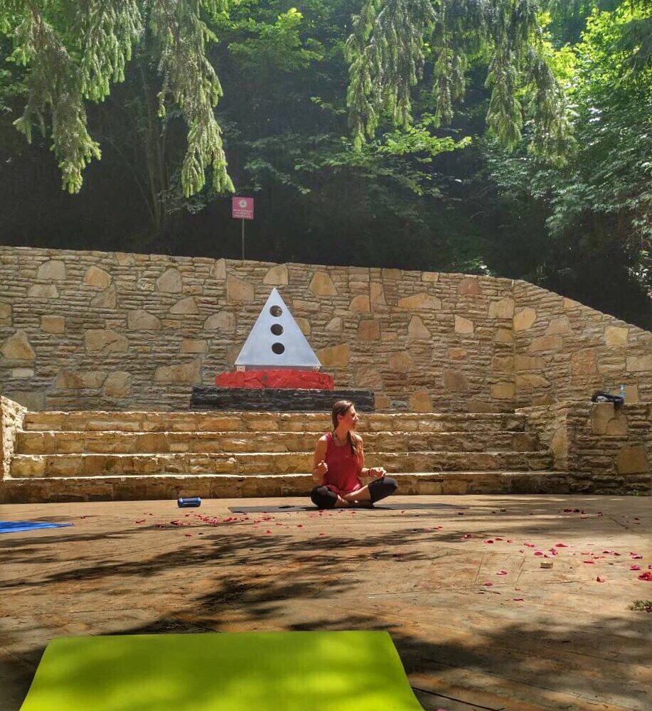 Woman meditating outdoors at the Bosnian Pyramid complex near a pyramid symbol sculpture.