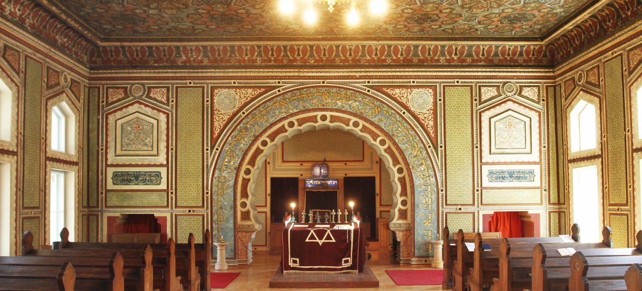 Interior view of the Ashkenazi Synagogue in Sarajevo, showcasing its richly decorated walls and ceiling, wooden pews, and the ornate ark.