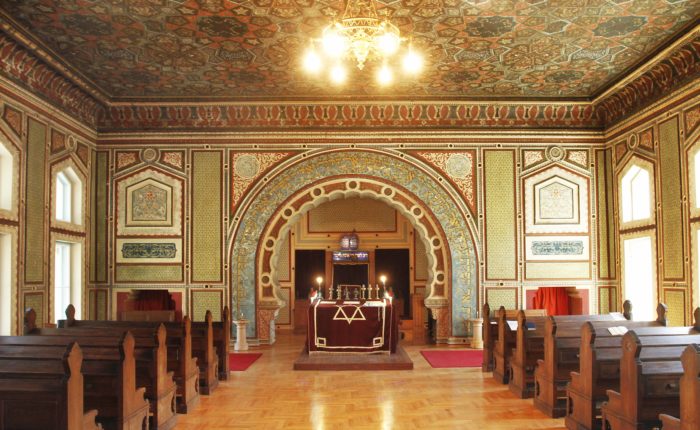Interior view of the Ashkenazi Synagogue in Sarajevo, showcasing its richly decorated walls and ceiling, wooden pews, and the ornate ark.