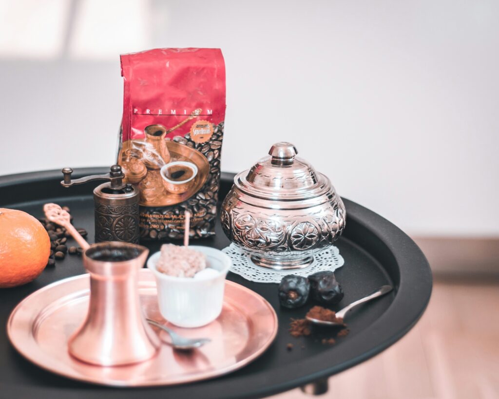 A beautifully arranged Bosnian coffee set with a copper džezva, sugar bowl, coffee grinder, dates, and coffee beans on a serving tray.