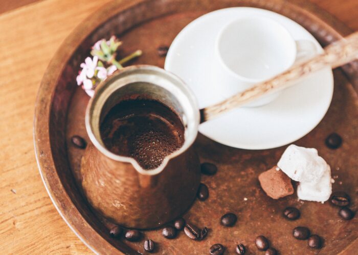 A copper džezva filled with freshly brewed Bosnian coffee on a tray with coffee beans, a white ceramic cup, and sweet treats.