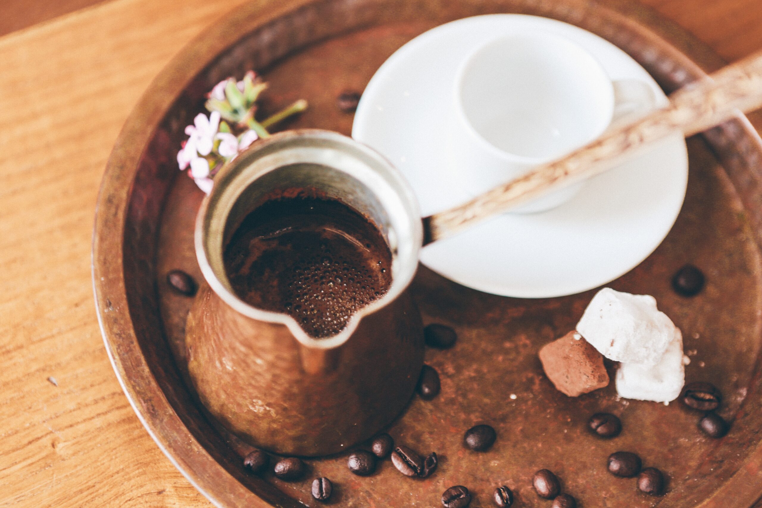 A copper džezva filled with freshly brewed Bosnian coffee on a tray with coffee beans, a white ceramic cup, and sweet treats.