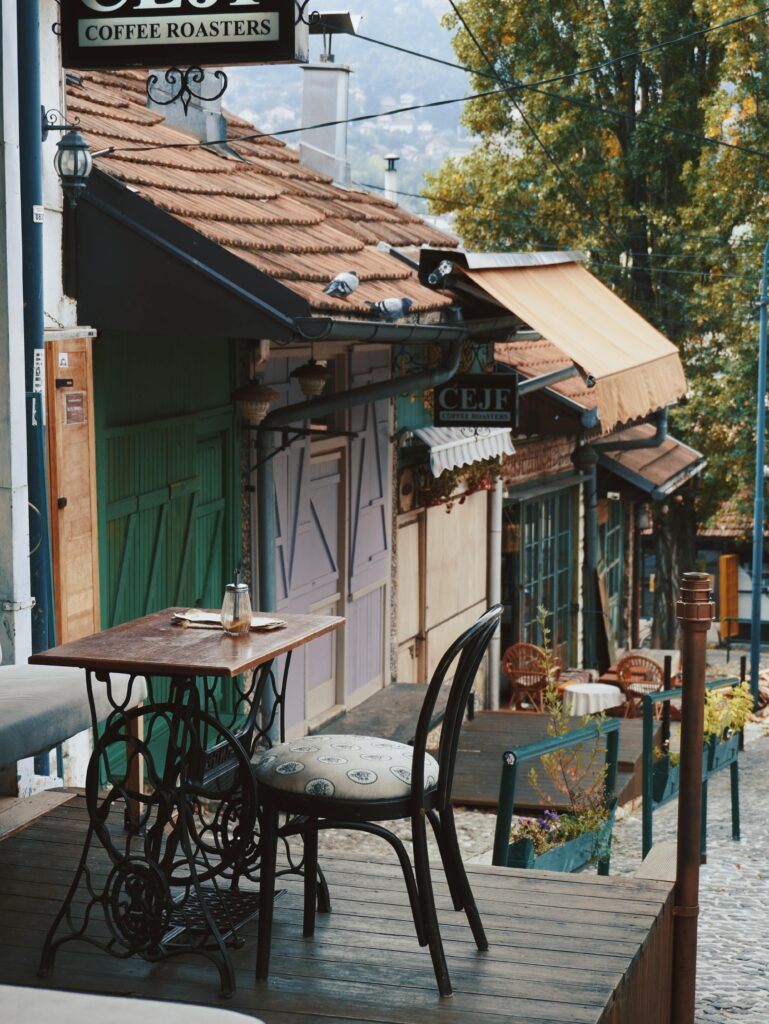 A charming outdoor seating area with a vintage table and chair in Sarajevo, overlooking a cobblestone street and quaint coffee roasters.