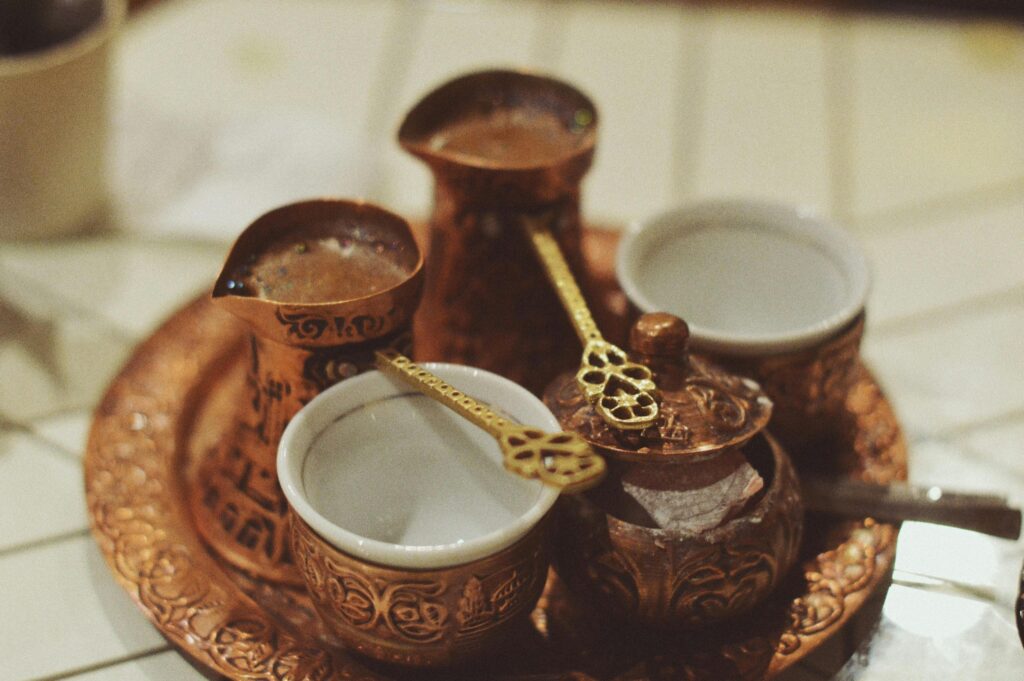 A traditional Bosnian coffee set featuring a copper džezva, two fildžans, and a sugar container on an intricately designed tray.